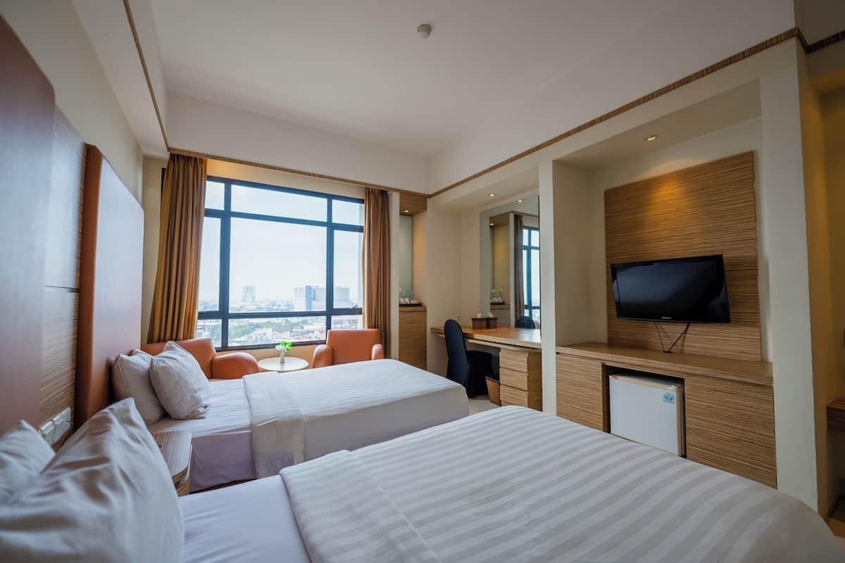 A hotel room with two beds, a desk, a chair, a television, and a window with a city view.