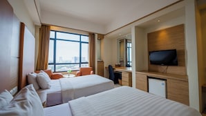 Habitación de hotel con dos camas, un escritorio, una silla, un televisor y una ventana con vista a la ciudad.