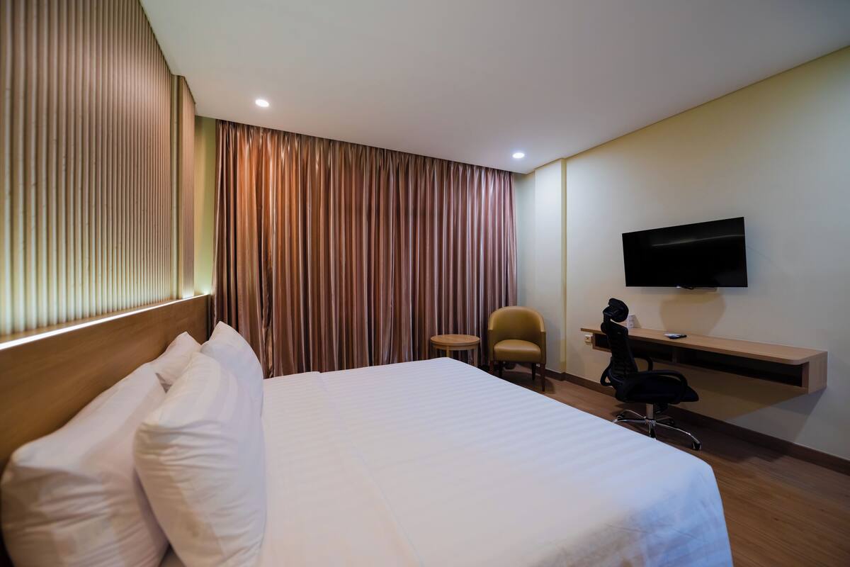 A hotel room with a large bed, a desk with a chair, a television, and a window with curtains.
