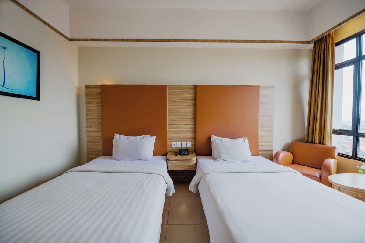 A hotel room with two beds, a nightstand, a chair, and a window with curtains.