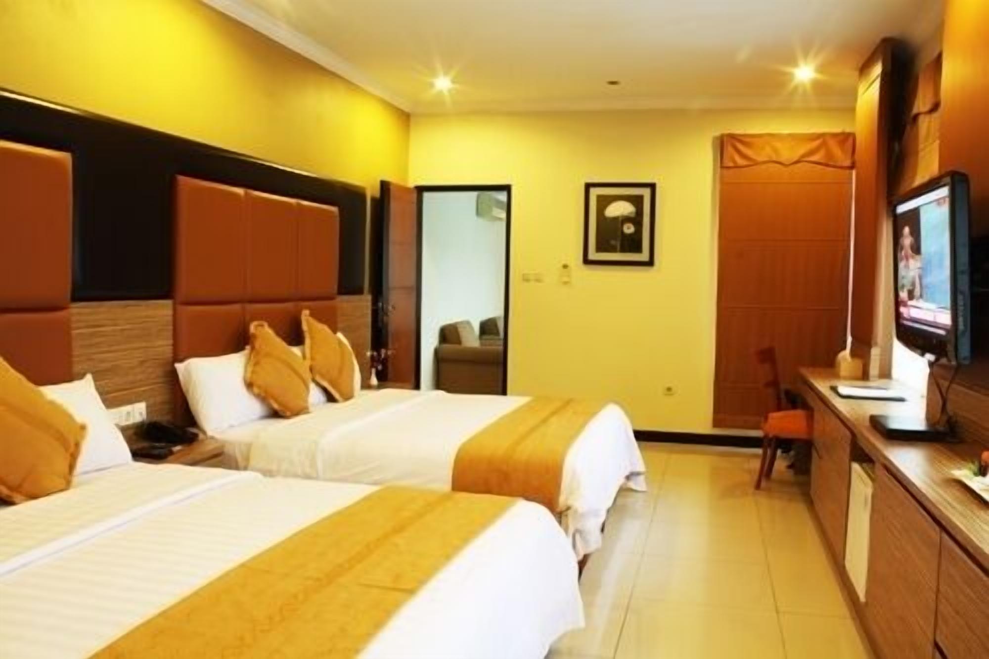 A hotel room with two beds, a desk with a computer, a television, and a door leading to another room.