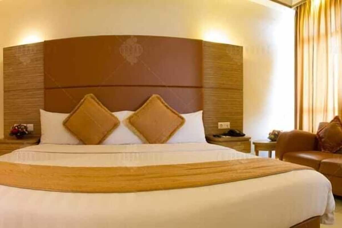 A hotel room with a large bed, a headboard, a nightstand, a sofa, and a window with curtains.