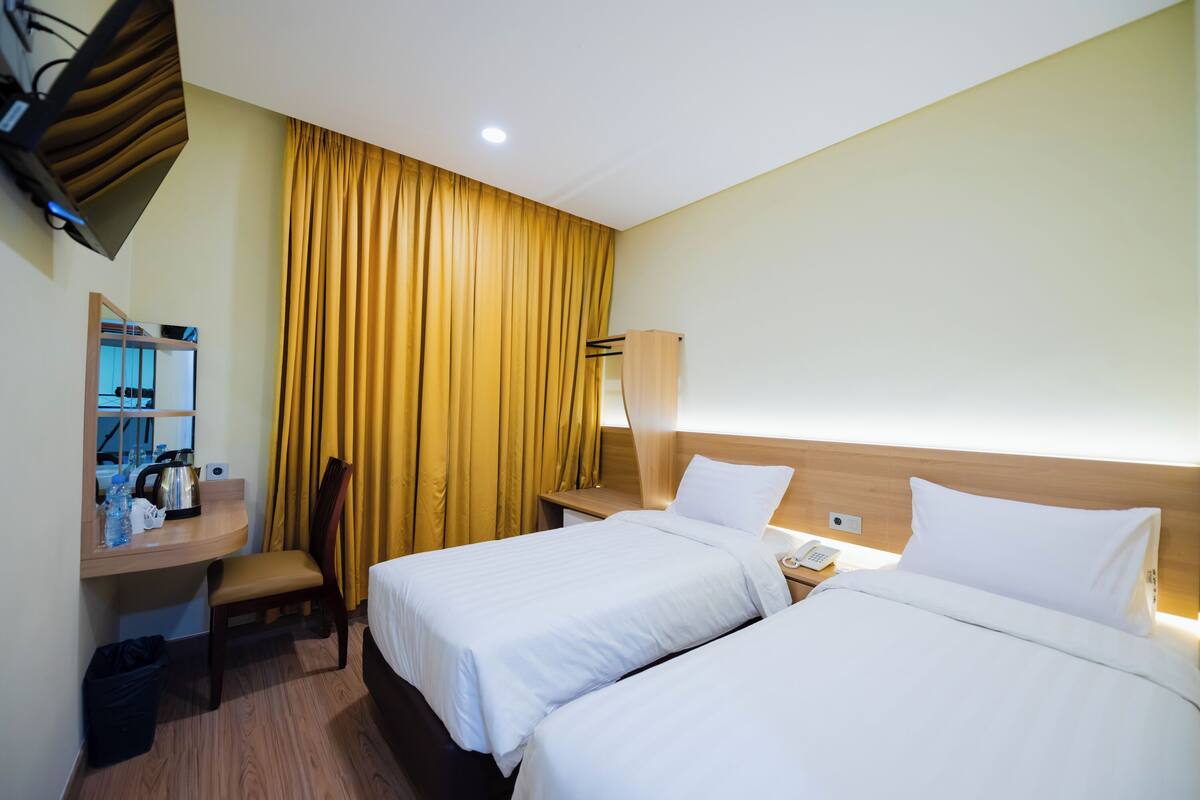 A hotel room with two beds, a desk with a chair, a mirror, a telephone, and a curtain.