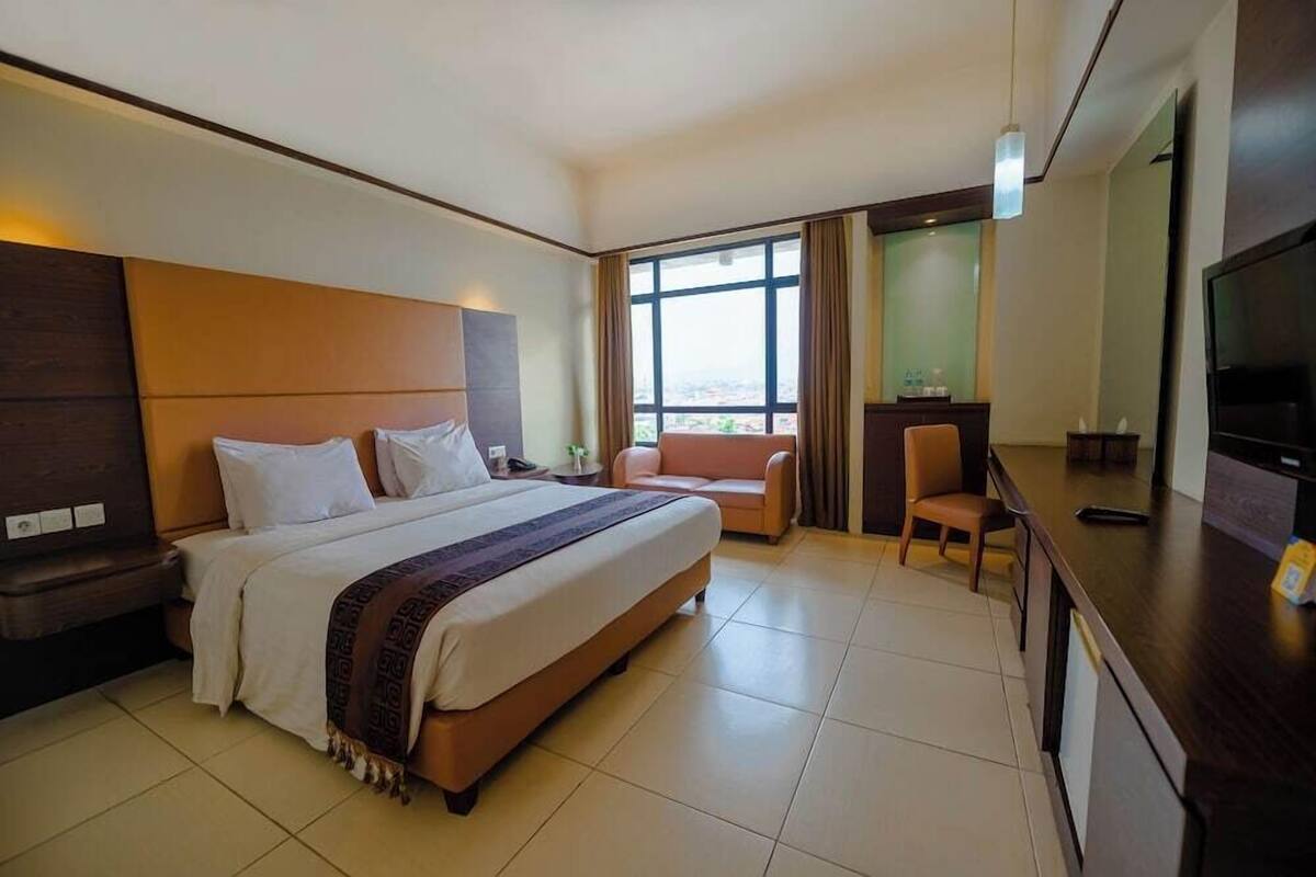 A hotel room with a large bed, a desk, a chair, a TV, and a window with curtains.