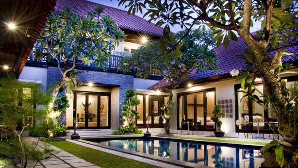 A modern house with a swimming pool, surrounded by lush greenery and well-lit outdoor areas.