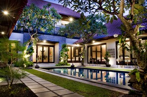 Una casa moderna con piscina, rodeada de exuberante vegetación y zonas exteriores bien iluminadas.