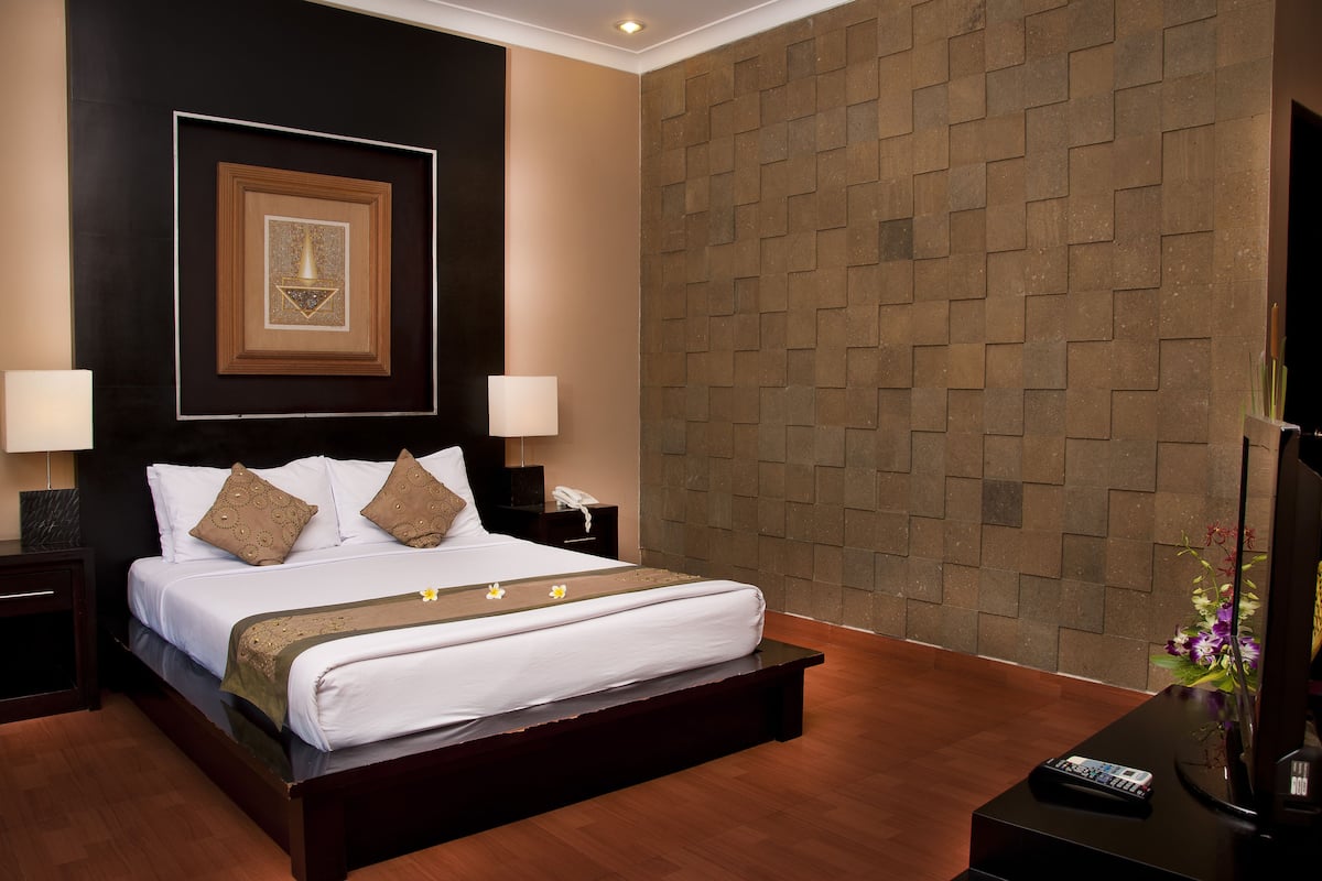 A hotel room with a large bed, two bedside tables, a wall-mounted TV, and a framed picture above the bed.