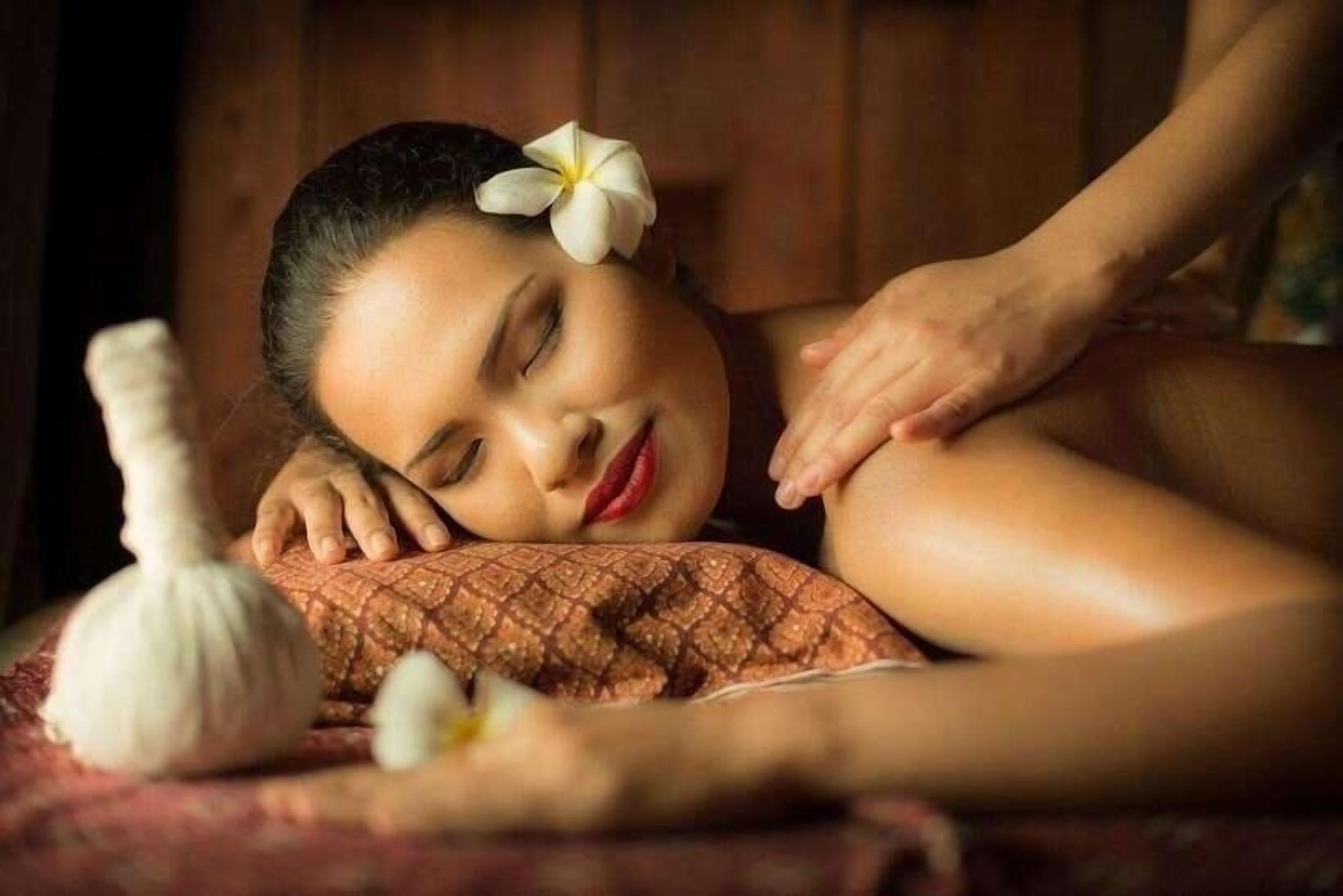 A person receiving a massage with a flower in their hair, a white object on the table, and a wooden background.