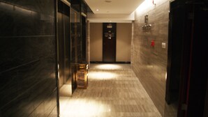 A hallway with marble flooring, a glass door on the left, and a door with a sign on the right.