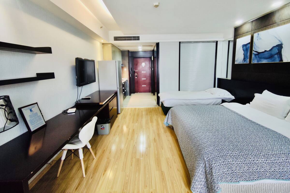 A hotel room with a bed, a desk with a chair, a television, and a door leading to another room.