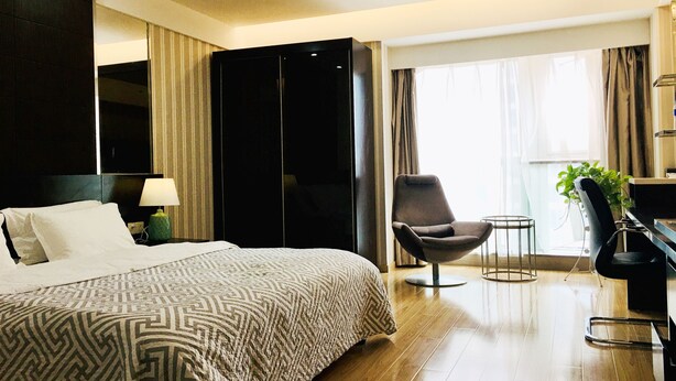 A hotel room with a large bed, a chair, a desk, and a plant.