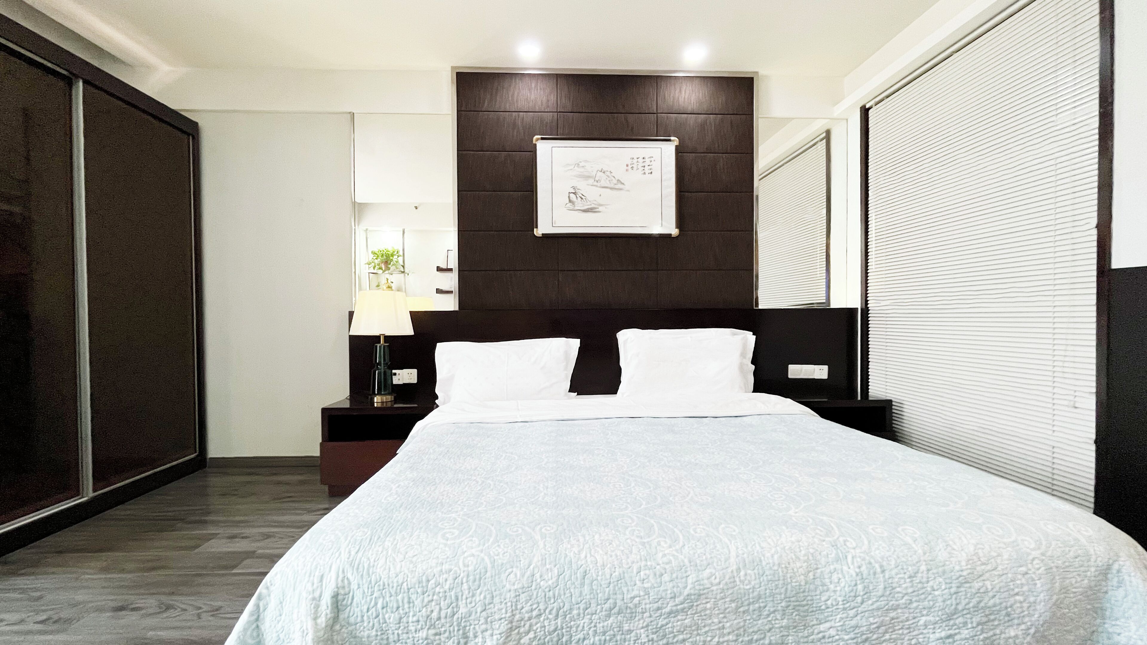 Habitación de hotel moderna con una cama grande, cabecera de madera oscura y una obra enmarcada sobre la cama.