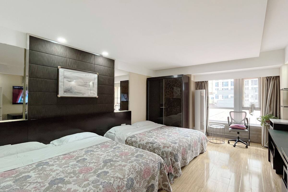 A hotel room with two beds, a desk, a chair, a TV, and a window with curtains.