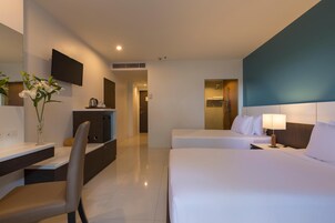 A hotel room with a bed, a desk, a chair, a TV, and a bathroom visible through an open door.