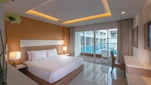 A modern hotel room with a large bed, bedside lamps, a desk, and a view of a swimming pool. - Chanalai Hillside Resort, Karon Beach (Karon)