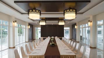 A conference room with a long table, white chairs, and chandeliers.