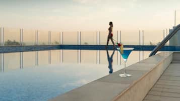 Zona junto a la piscina con vista despejada, área de bar con una copa de martini, y una persona caminando.
