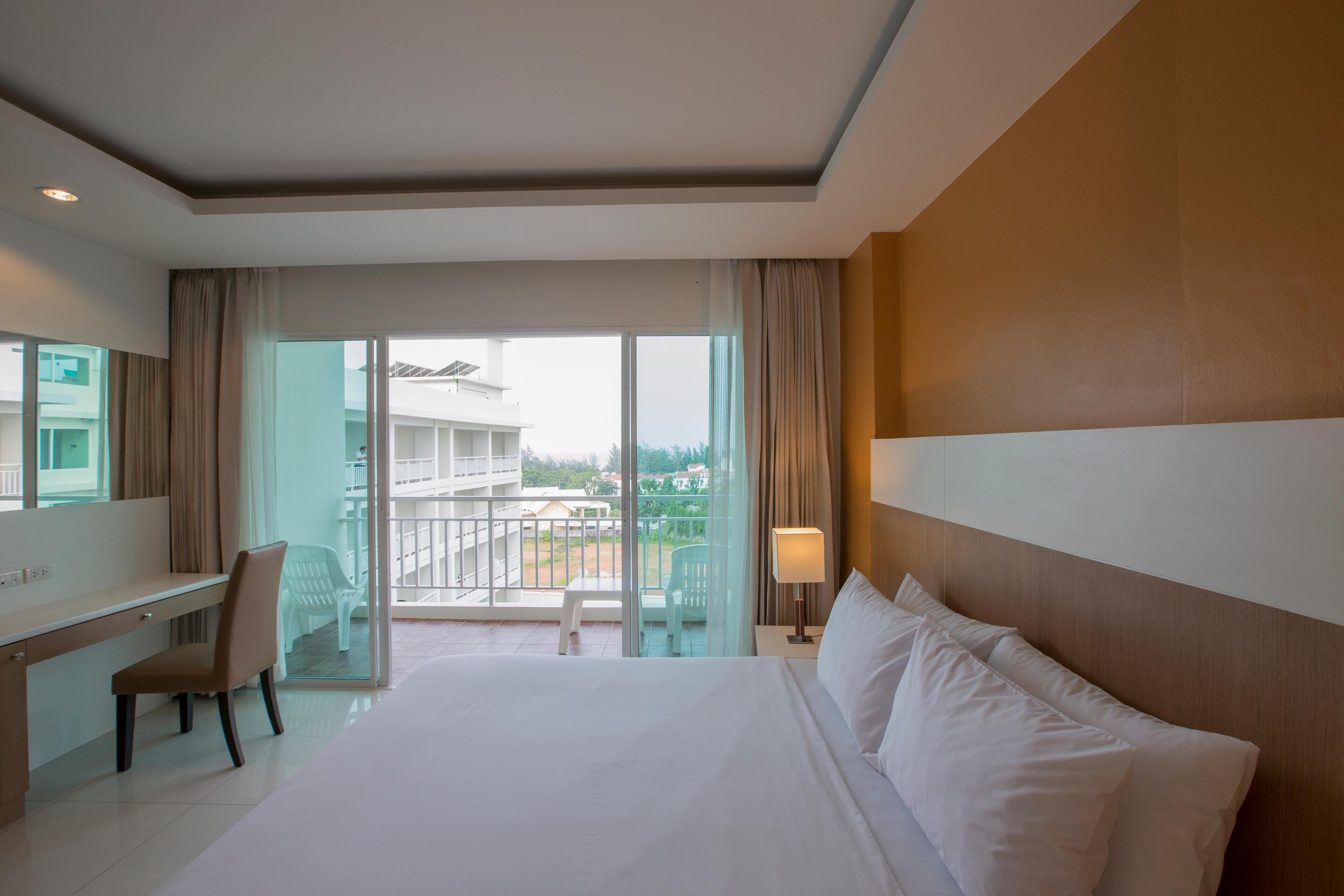 Habitación de hotel con una cama grande, un escritorio, una silla, un balcón con vistas a edificios y un ventanal amplio.