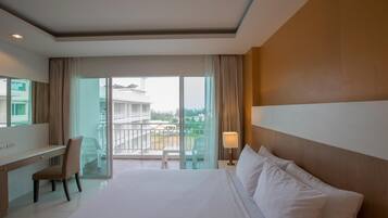 Habitación de hotel con una cama grande, un escritorio, una silla, un balcón con vistas a edificios y un ventanal amplio.