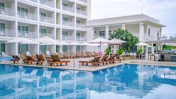 A swimming pool with lounge chairs and umbrellas, surrounded by a multi-story building with balconies.