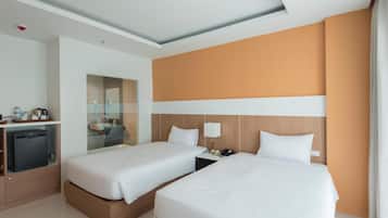 A hotel room with two beds, a minibar, a desk, and a mirror.