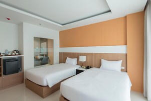 A hotel room with two beds, a minibar, a desk, and a mirror.