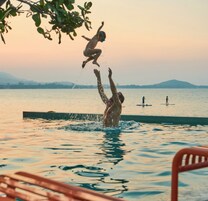 A person jumping into a pool with another person in the background.