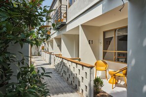 A modern building with numbered rooms E1, E3, and E13, a wooden balcony, and yellow chairs outside. - Escape Beach Resort (Koh Samui)
