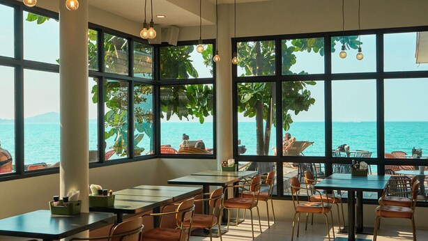 A restaurant with large windows overlooking the sea, featuring tables and chairs arranged for dining. - Escape Beach Resort (Koh Samui)
