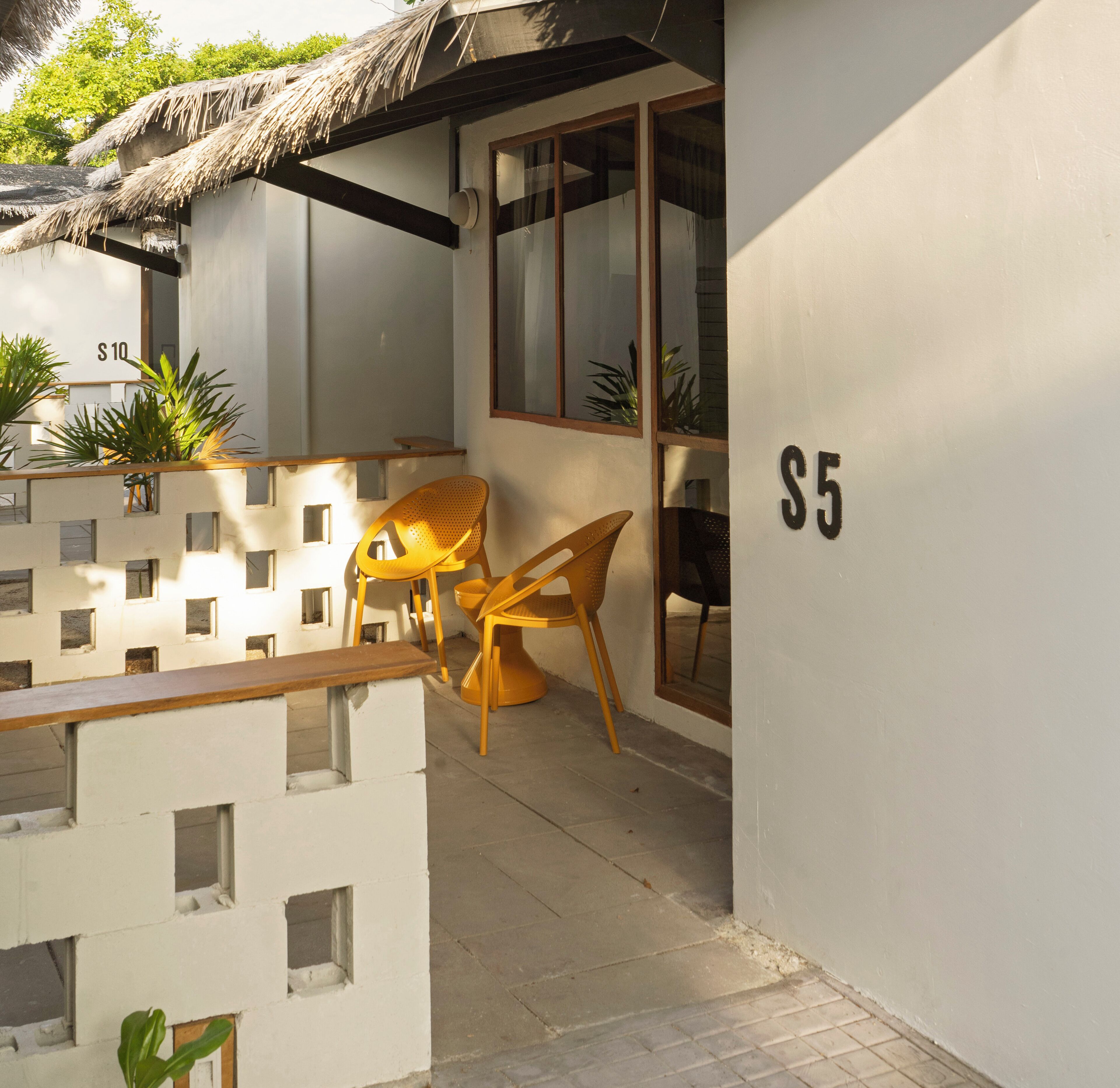 A balcony with a thatched roof, a wooden bench, and two yellow chairs.