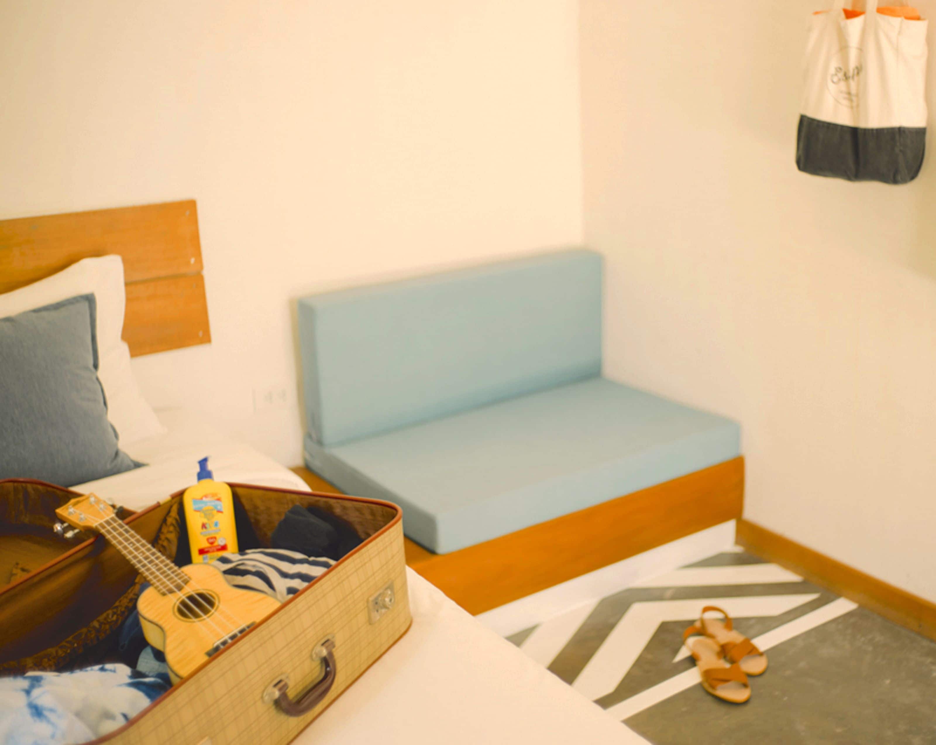 A room with a bed, a blue sofa, a suitcase, a guitar, and a pair of sandals.