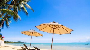 A beach with two lounge chairs and two umbrellas, a clear blue sky, and a calm sea. - Escape Beach Resort (Koh Samui)