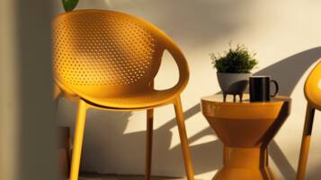 A yellow chair and a small table with a potted plant and a black mug on it, positioned against a white wall.