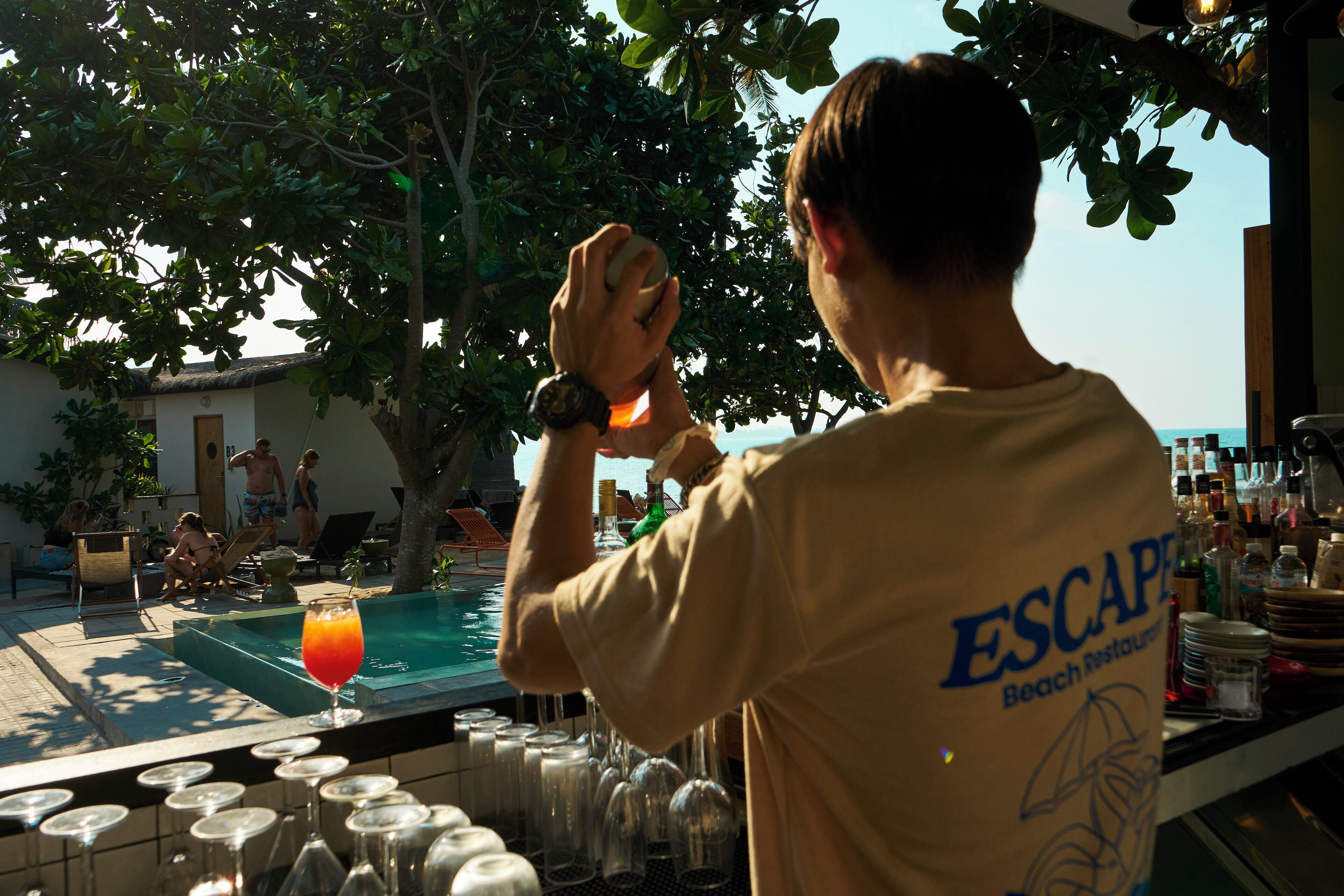 A bartender preparing a drink at a poolside bar with a view of the ocean.