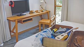 A bedroom with a bed, a wooden desk with a TV, a guitar, and a suitcase.