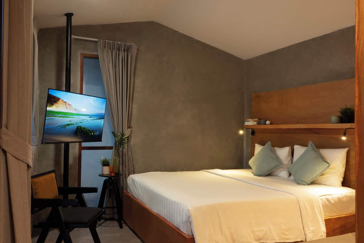A bedroom with a bed, a TV, a small table with a plant, and a window with curtains.