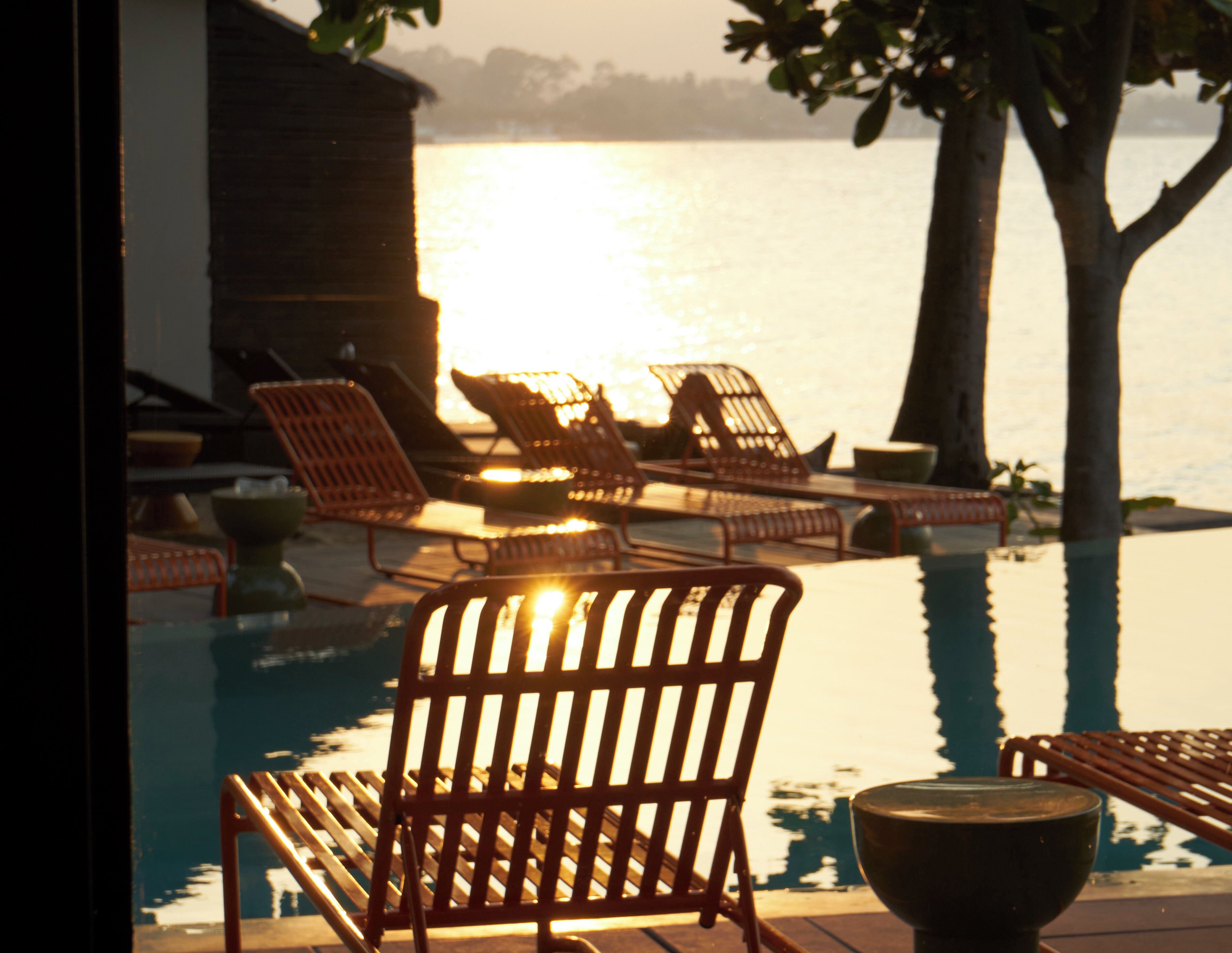 Zona junto a la piscina con sillones de descanso y vistas al agua.