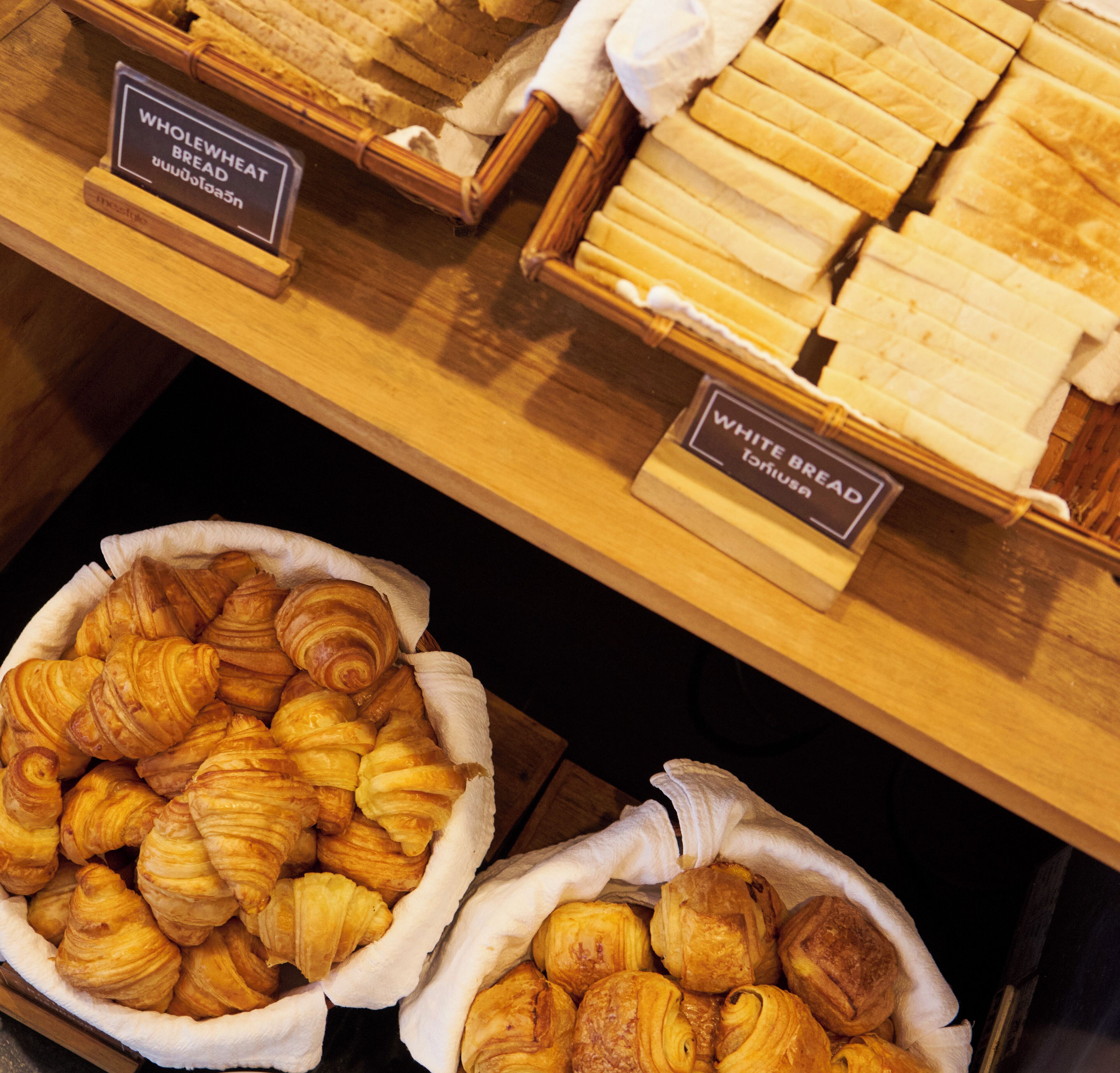 Een bakkerijvitrine met brood en croissants, voorzien van labels.