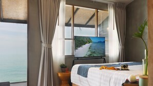 A bedroom with a large window, a bed, a bedside table with a plant, and a camera on the bed. - Escape Beach Resort (Koh Samui)