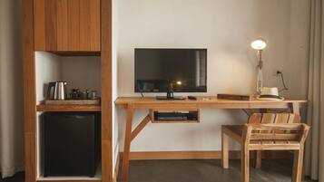A compact room with a wooden desk, a television, a small refrigerator, and a chair.