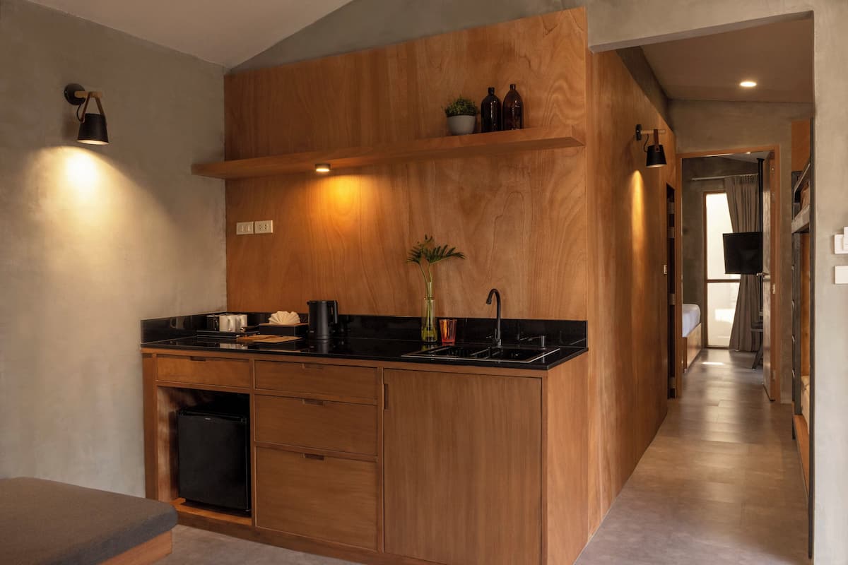 A modern kitchen with wooden cabinetry, a black countertop, and a built-in sink. There is a small plant on the countertop and a shelf above the sink.