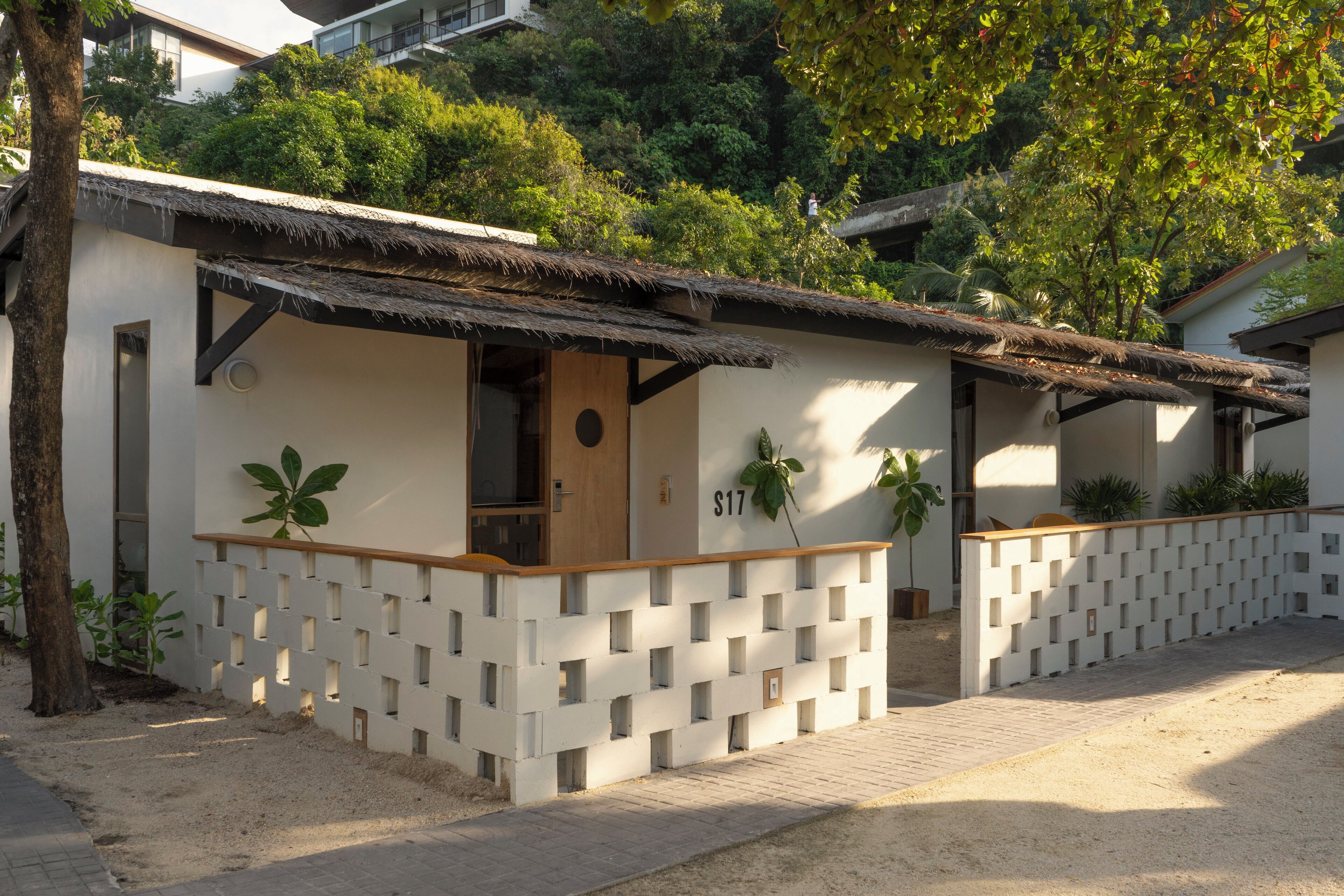 A modern building with a thatched roof, a number 'S17' on the wall, and a lattice fence.