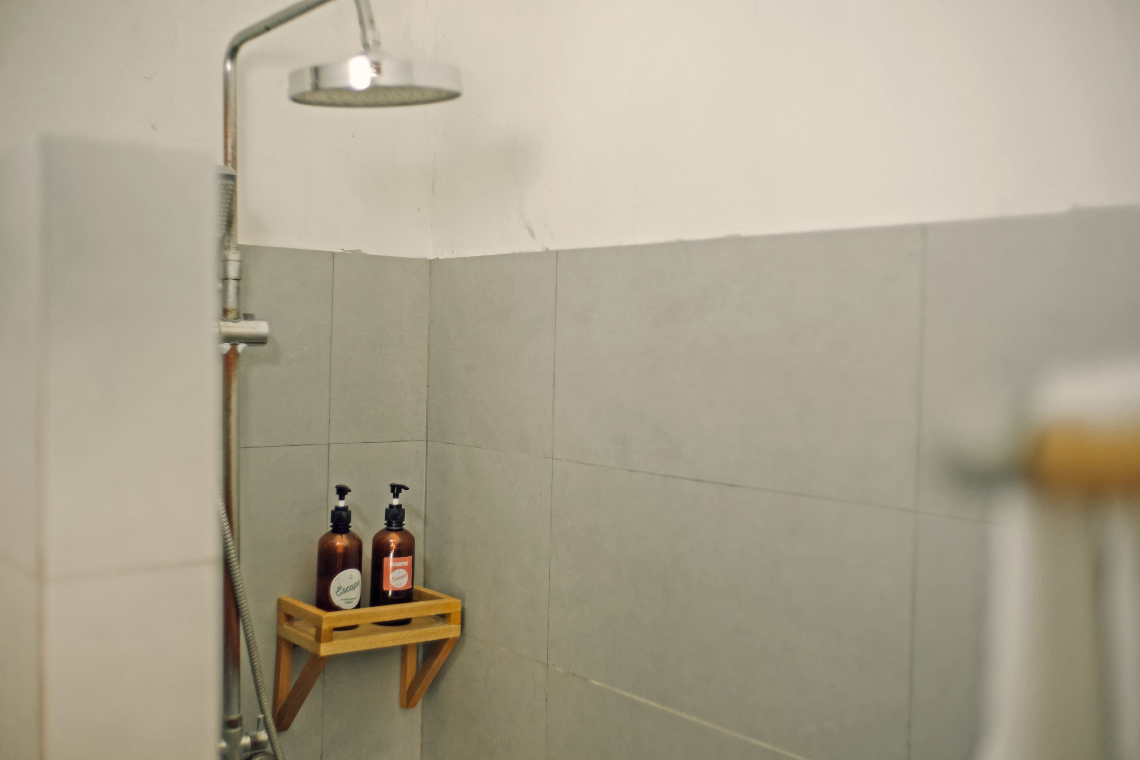 Zona de ducha con cabezal de ducha de mano, un estante de madera con dos botellas y pared con azulejos.