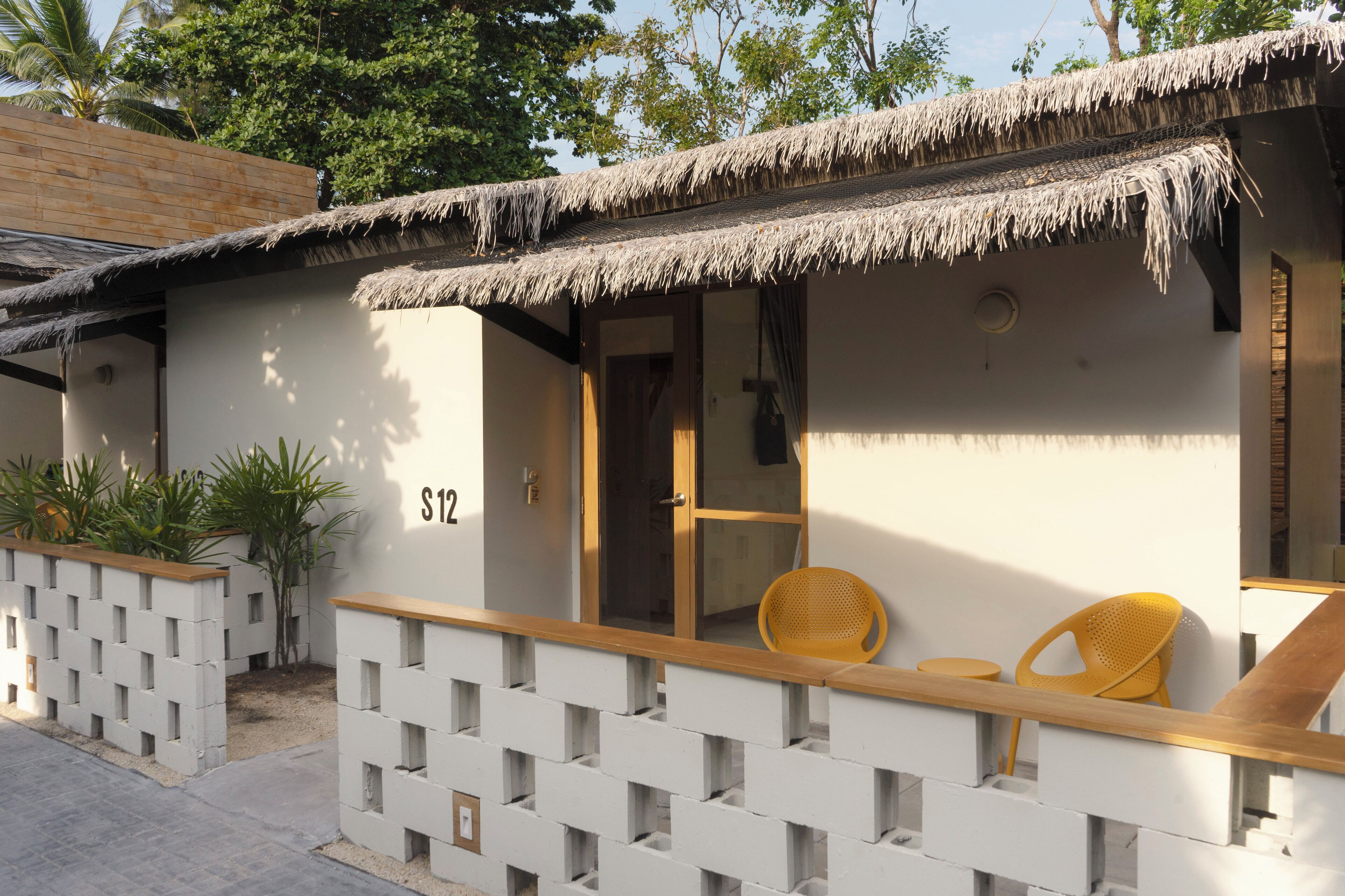 A small, single-room structure with a thatched roof, a wooden bench, and two chairs.