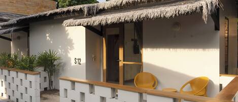 A small, single-room structure with a thatched roof, a wooden bench, and two chairs.