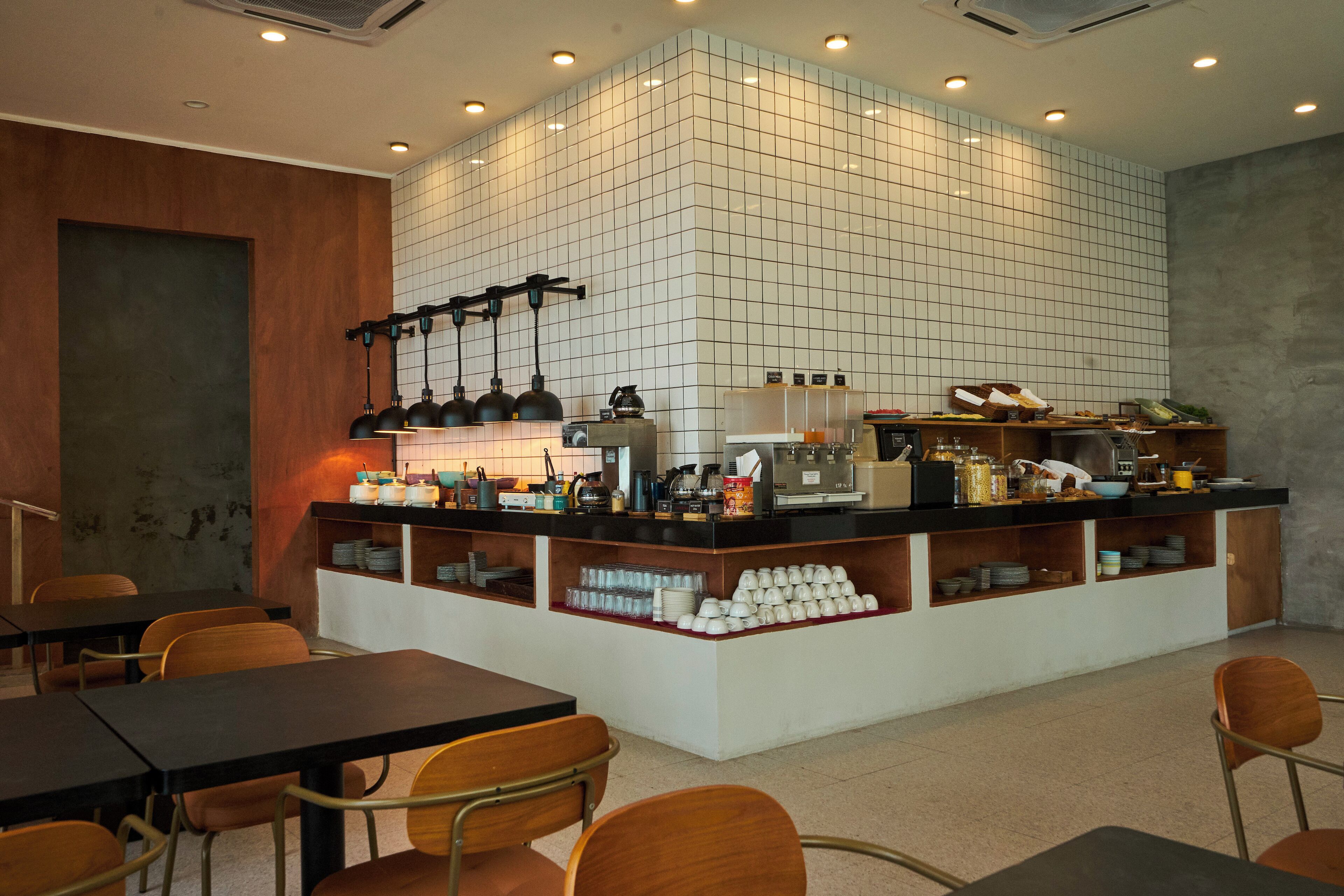 A modern cafe with a central counter, seating area, and kitchen visible.
