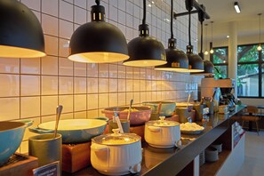 A buffet area with various dishes and cooking utensils, a tiled backsplash, and hanging pendant lights. - Escape Beach Resort (Koh Samui)