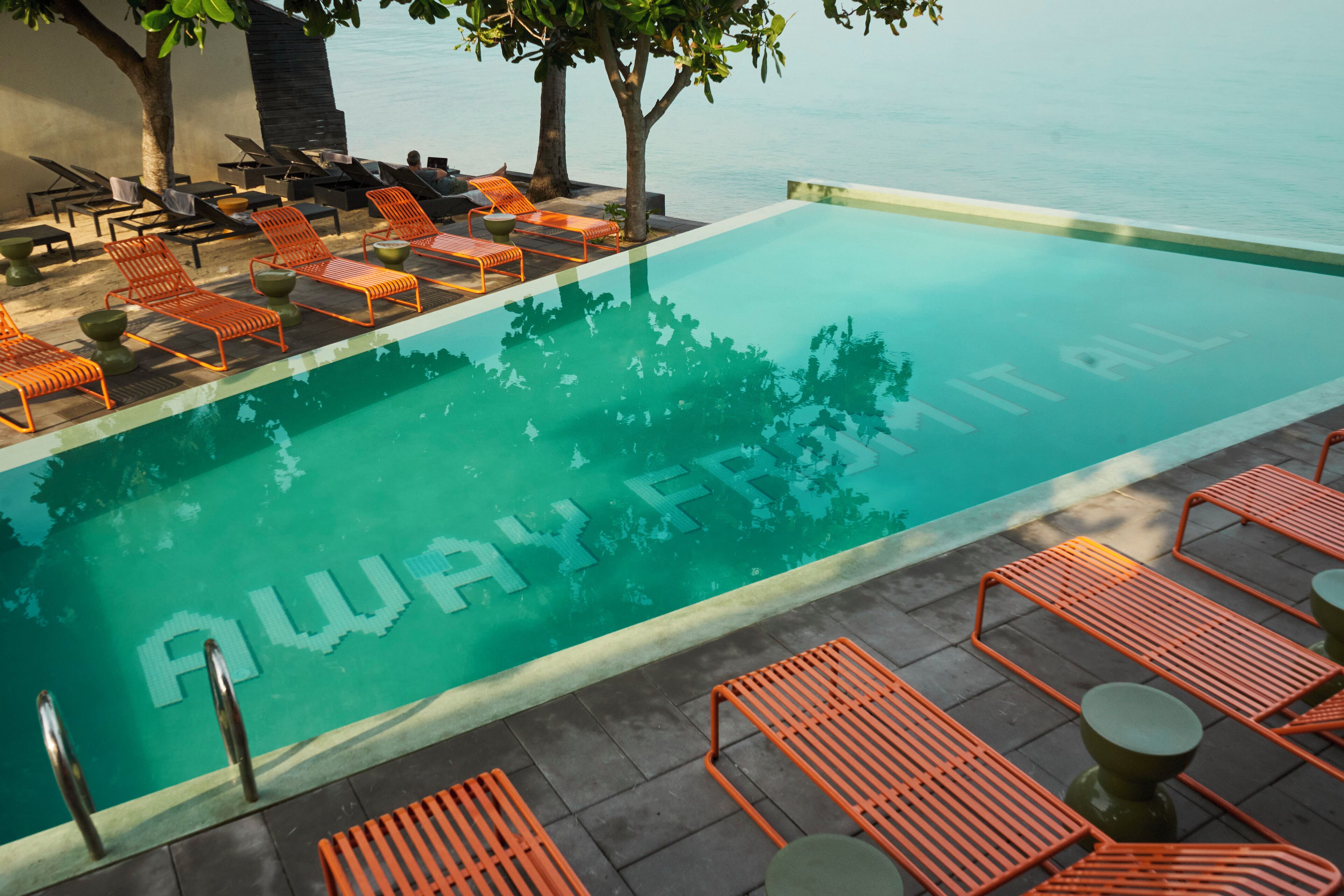 Zona junto a la piscina con sillas reclinables anaranjadas y una piscina de superficie reflectante.