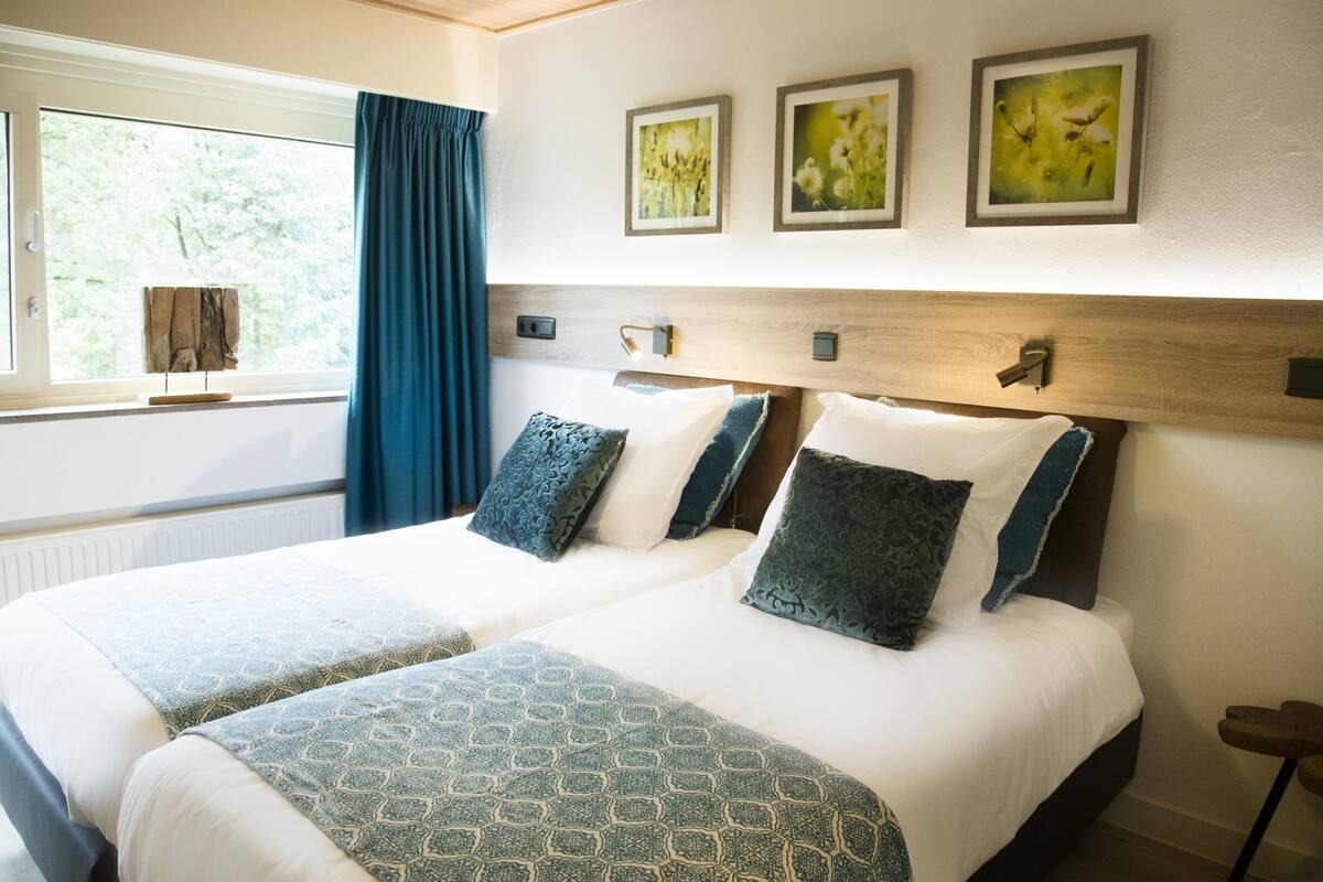 Uma cama de casal com roupa de cama estampada, uma cabeceira de madeira e três quadros florais na parede.