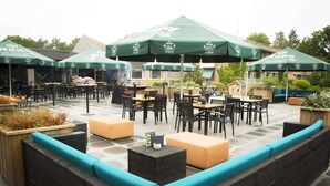 An outdoor patio area with tables and chairs under green umbrellas, surrounded by stone walls and wooden planters.